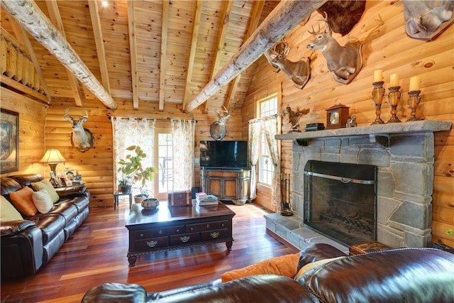 living room featuring beam ceiling, dark wood finished floors, wood ceiling, wooden walls, and a stone fireplace