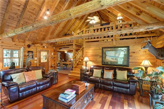 living room featuring wood walls, wood finished floors, wood ceiling, a ceiling fan, and stairs