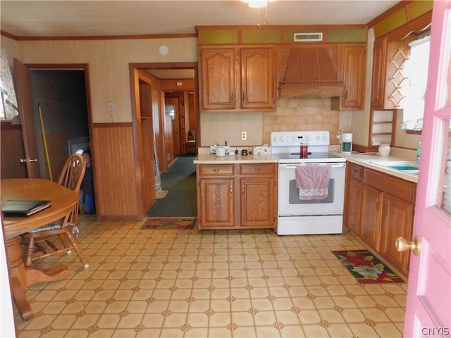 kitchen with electric stove, a wainscoted wall, crown molding, light floors, and premium range hood