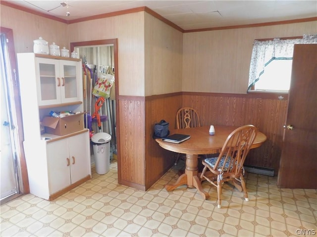 dining area with a wainscoted wall, a baseboard heating unit, wood walls, ornamental molding, and light floors