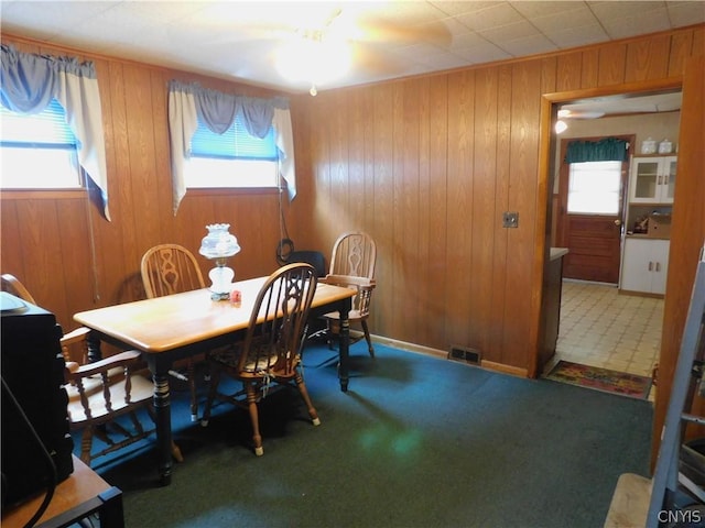 dining area featuring carpet floors, a wealth of natural light, visible vents, and wooden walls