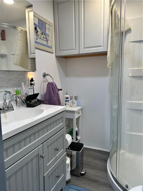 bathroom featuring tasteful backsplash, a shower with door, vanity, and wood-type flooring