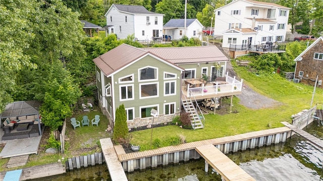 rear view of property featuring a deck with water view and a lawn