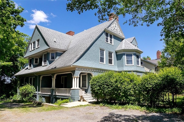 victorian home with a shingled roof, covered porch, and a chimney