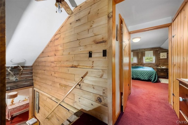 corridor with dark colored carpet, lofted ceiling, and wood walls