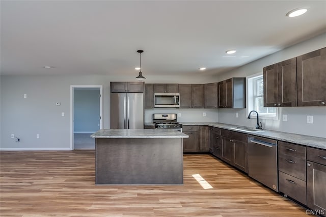 kitchen with decorative light fixtures, light hardwood / wood-style floors, stainless steel appliances, a center island, and sink