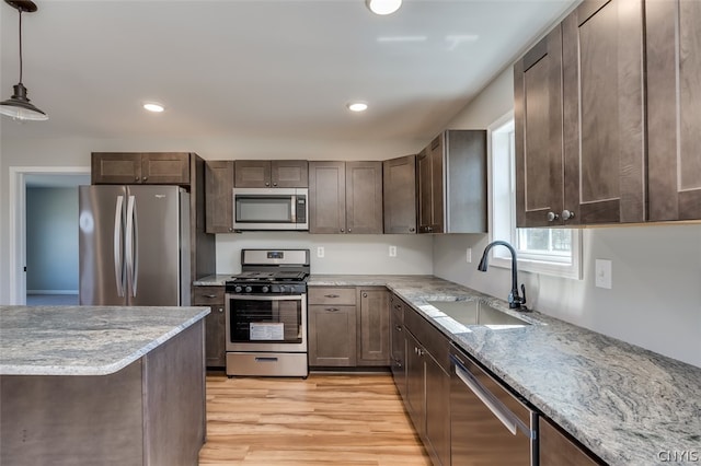 kitchen featuring decorative light fixtures, stainless steel appliances, light stone countertops, light wood-type flooring, and sink