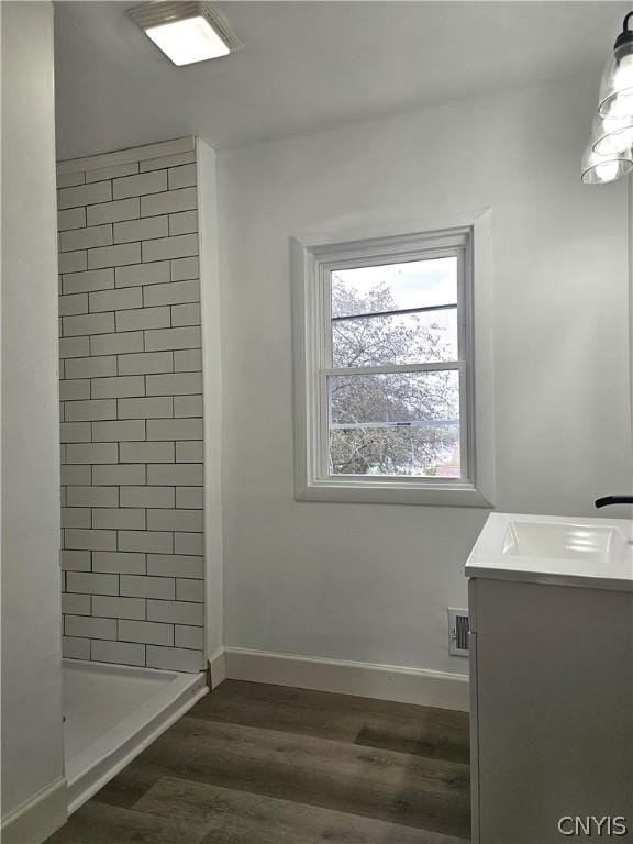 bathroom with tiled shower, vanity, and wood-type flooring