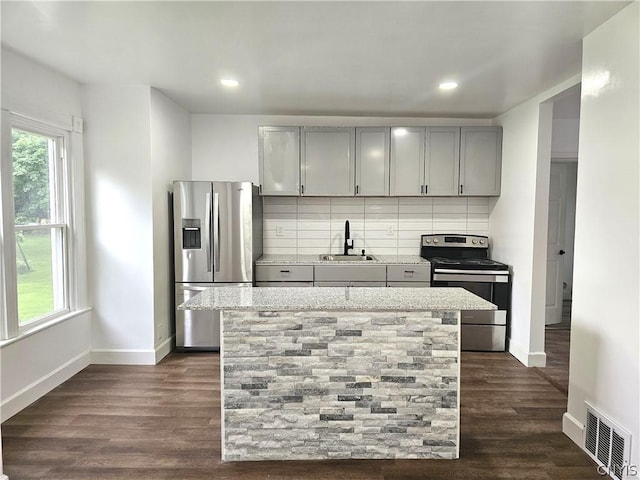 kitchen with gray cabinets, appliances with stainless steel finishes, sink, backsplash, and a center island