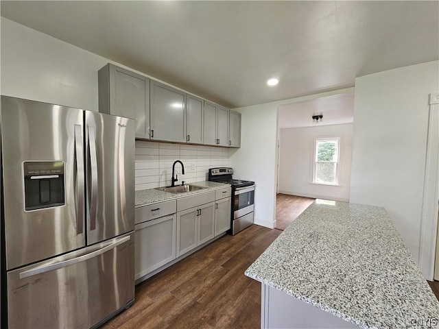 kitchen featuring sink, gray cabinetry, light stone counters, stainless steel appliances, and decorative backsplash