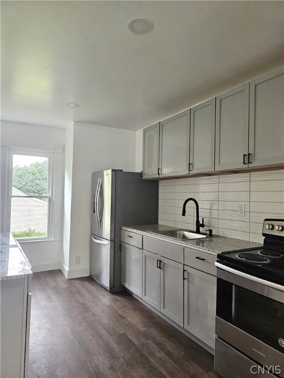 kitchen with sink, appliances with stainless steel finishes, light stone counters, dark hardwood / wood-style flooring, and decorative backsplash