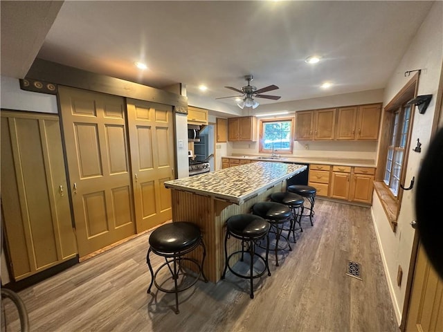 kitchen featuring a kitchen bar, ceiling fan, sink, wood-type flooring, and a kitchen island