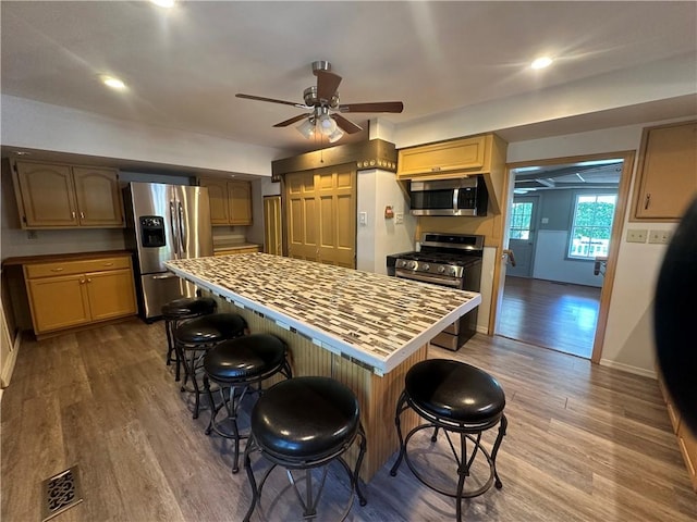 kitchen featuring ceiling fan, wood-type flooring, a breakfast bar area, and appliances with stainless steel finishes