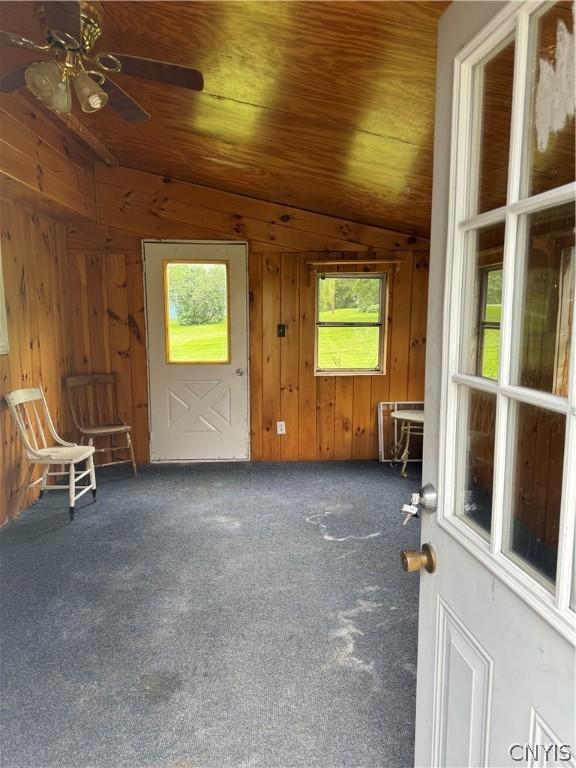 carpeted spare room with wooden ceiling, wooden walls, ceiling fan, and lofted ceiling