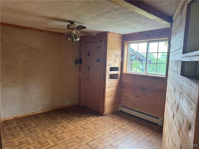 empty room featuring ceiling fan, parquet floors, a textured ceiling, wooden walls, and a baseboard radiator