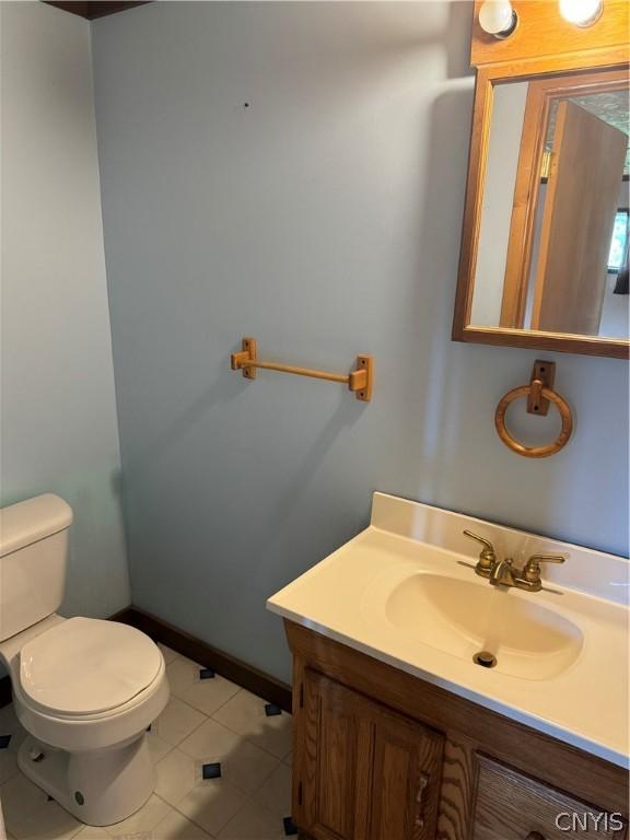 half bath featuring tile patterned floors, toilet, and vanity