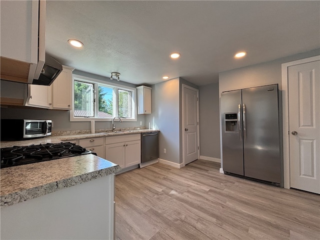 kitchen with a textured ceiling, white cabinetry, light hardwood / wood-style flooring, stainless steel appliances, and extractor fan