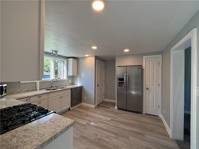 kitchen featuring sink, a textured ceiling, white cabinetry, appliances with stainless steel finishes, and light wood-type flooring