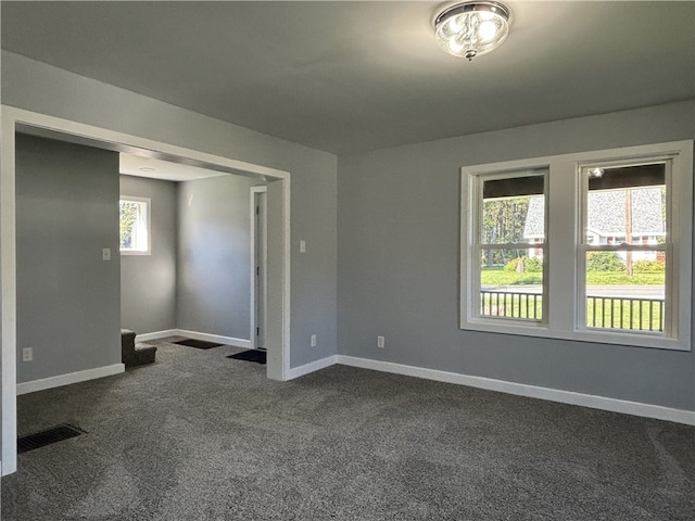 empty room with dark colored carpet and a healthy amount of sunlight