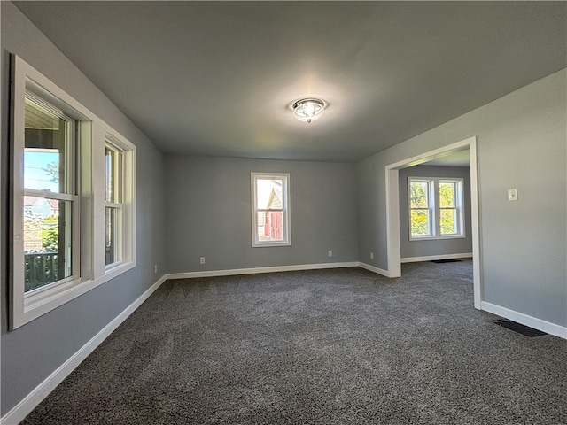 unfurnished room featuring dark colored carpet and a healthy amount of sunlight