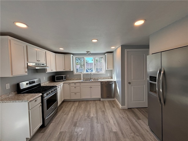 kitchen with light hardwood / wood-style floors, sink, white cabinets, appliances with stainless steel finishes, and light stone countertops