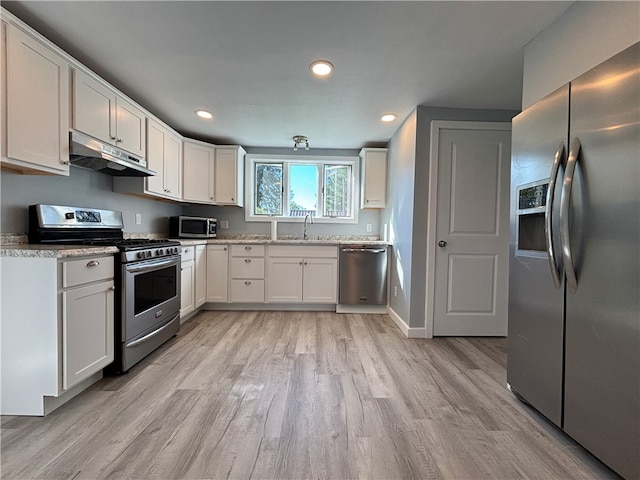 kitchen with light stone countertops, white cabinets, light hardwood / wood-style floors, and appliances with stainless steel finishes