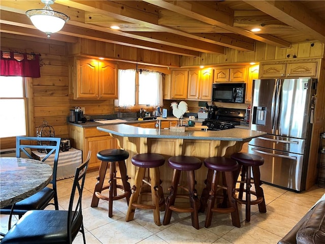 kitchen featuring light tile patterned flooring, an island with sink, wooden walls, and black appliances