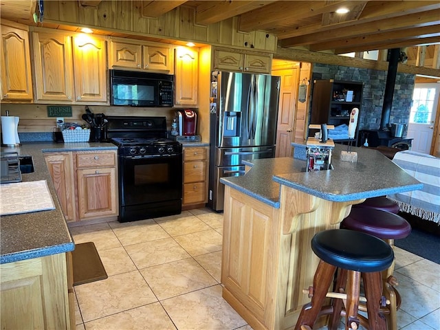 kitchen featuring black appliances, beam ceiling, light tile patterned floors, a wood stove, and a kitchen island