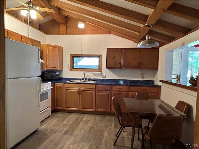 kitchen with dark countertops, vaulted ceiling with beams, light wood-style floors, white appliances, and a sink