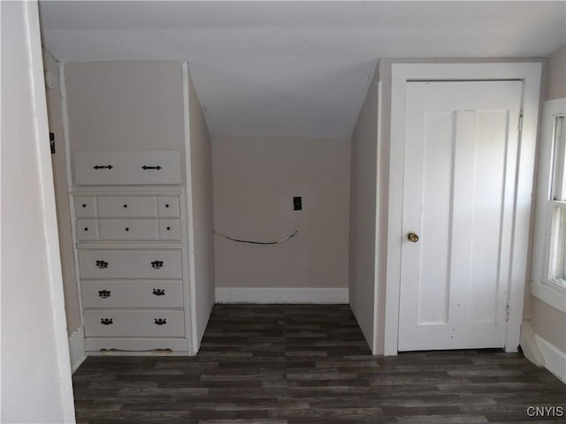 corridor with dark wood-style flooring, baseboards, and vaulted ceiling