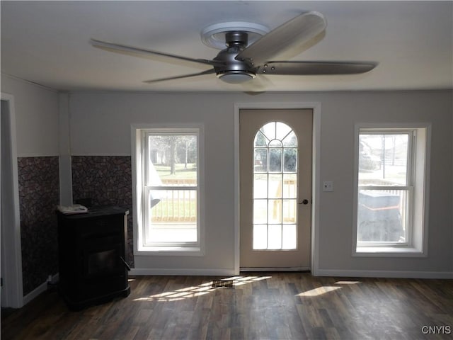doorway to outside featuring dark wood-type flooring, a healthy amount of sunlight, a wood stove, and a ceiling fan