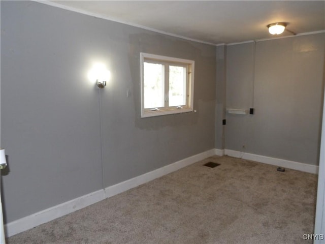 carpeted spare room featuring visible vents, baseboards, and crown molding