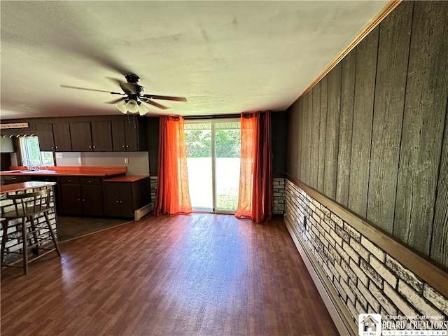 interior space with dark hardwood / wood-style flooring, baseboard heating, wooden walls, and ceiling fan