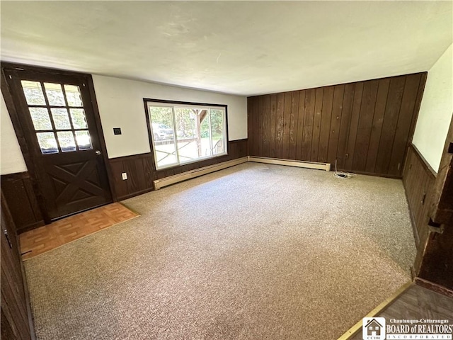 unfurnished living room with parquet floors, baseboard heating, a wealth of natural light, and wooden walls