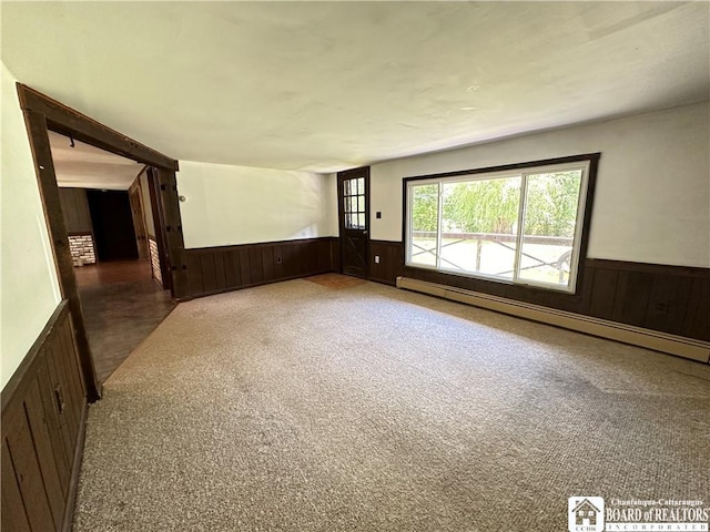 carpeted empty room featuring a baseboard radiator and wood walls