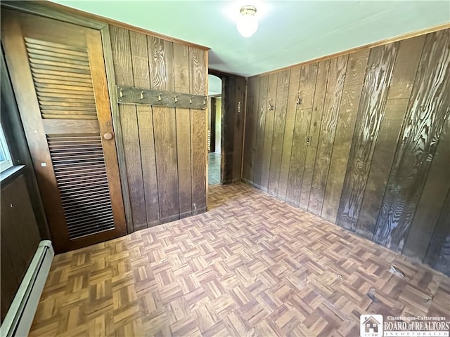 spare room featuring light parquet floors, a baseboard heating unit, and wood walls