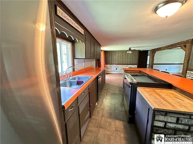 kitchen with butcher block counters, ceiling fan, sink, black dishwasher, and brick wall