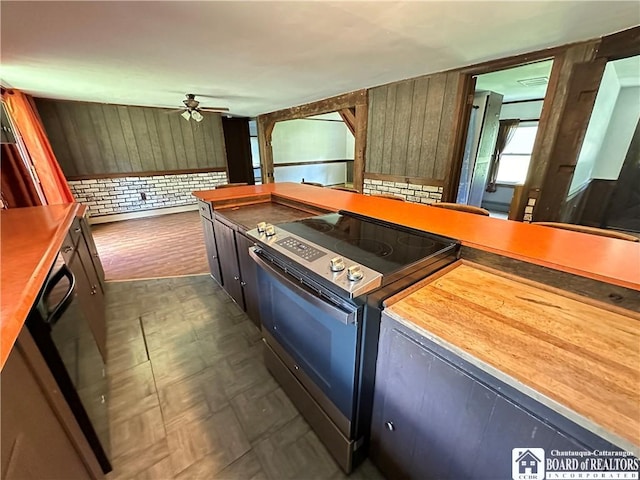 kitchen with ceiling fan, black electric range oven, and wood walls