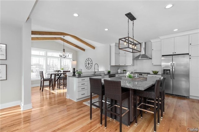 kitchen with stainless steel refrigerator with ice dispenser, wall chimney range hood, vaulted ceiling with beams, decorative backsplash, and kitchen peninsula