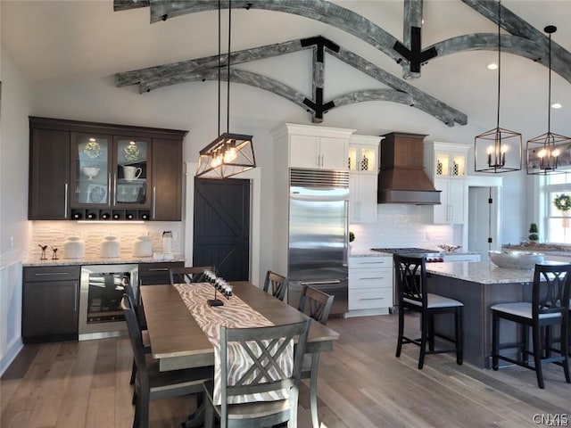 kitchen featuring custom exhaust hood, white cabinetry, built in refrigerator, dark brown cabinets, and beverage cooler