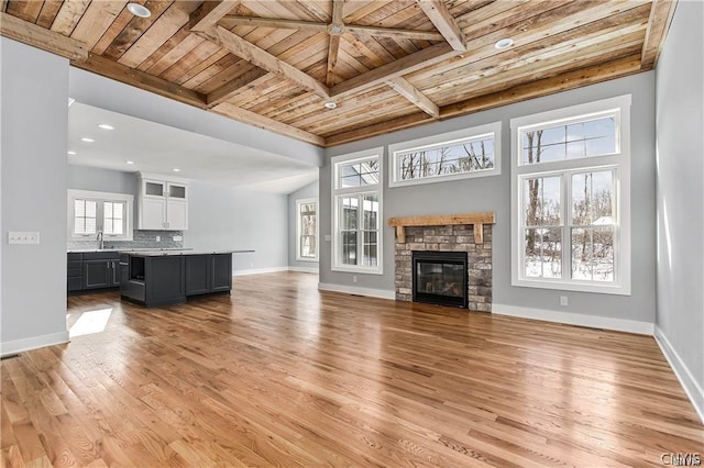 unfurnished living room featuring light hardwood / wood-style floors, wooden ceiling, a fireplace, beam ceiling, and sink