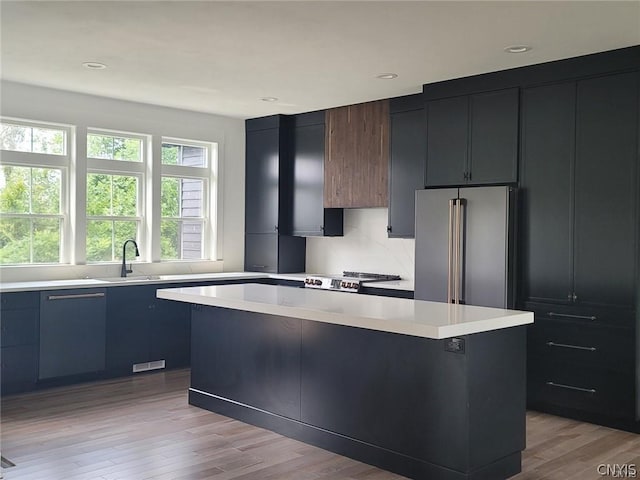 kitchen with high end fridge, a center island, stove, light hardwood / wood-style flooring, and sink