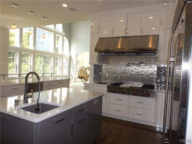 kitchen featuring white cabinets, decorative light fixtures, sink, backsplash, and light stone counters