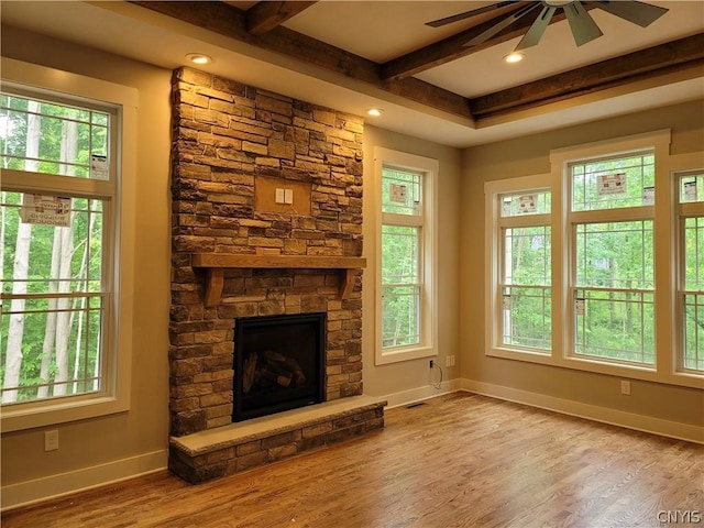 unfurnished living room with ceiling fan, a healthy amount of sunlight, beamed ceiling, and a fireplace