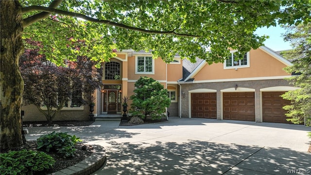 view of front of home featuring driveway, stone siding, an attached garage, and stucco siding