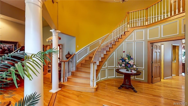 stairs with a towering ceiling, ornate columns, and wood finished floors