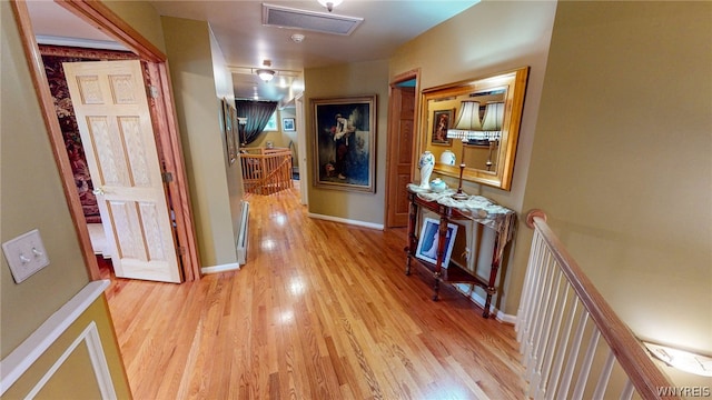 hall featuring baseboards, light wood-style flooring, and an upstairs landing