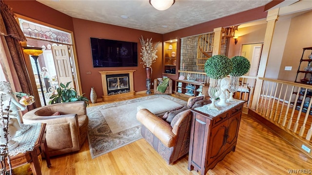 living room with light wood-type flooring, a glass covered fireplace, decorative columns, and a textured ceiling