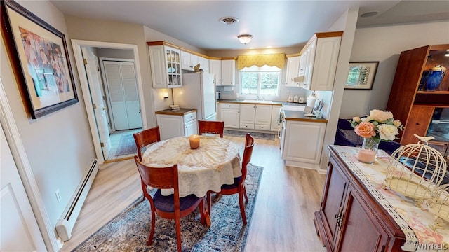 dining area featuring light wood finished floors, baseboard heating, visible vents, and baseboards