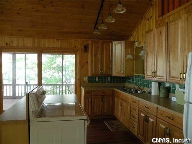 kitchen featuring lofted ceiling, wooden walls, backsplash, sink, and white fridge